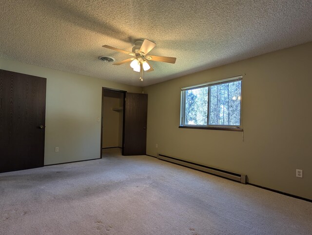 unfurnished bedroom with a baseboard heating unit, light colored carpet, a textured ceiling, a closet, and a ceiling fan
