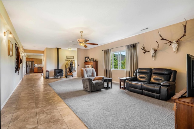 living room featuring light tile patterned floors, a wood stove, baseboards, and a ceiling fan
