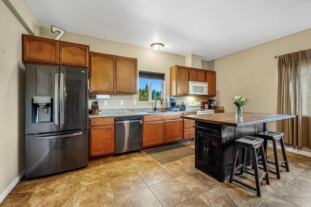 kitchen with appliances with stainless steel finishes, a sink, brown cabinetry, and a breakfast bar