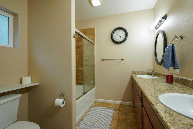 bathroom with toilet, double vanity, tile patterned flooring, baseboards, and combined bath / shower with glass door
