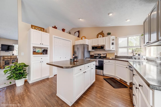 kitchen featuring stainless steel appliances, a sink, vaulted ceiling, light wood-type flooring, and a kitchen island
