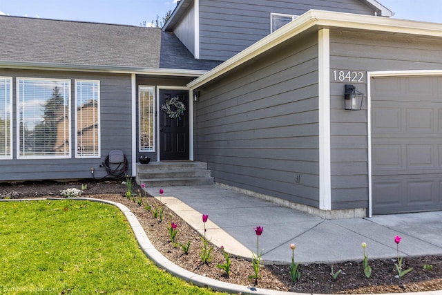 view of exterior entry featuring a garage, a shingled roof, and a lawn