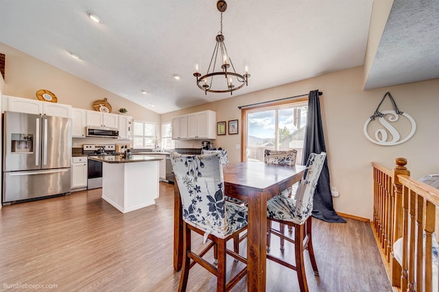 dining space featuring a chandelier, vaulted ceiling, wood finished floors, and baseboards