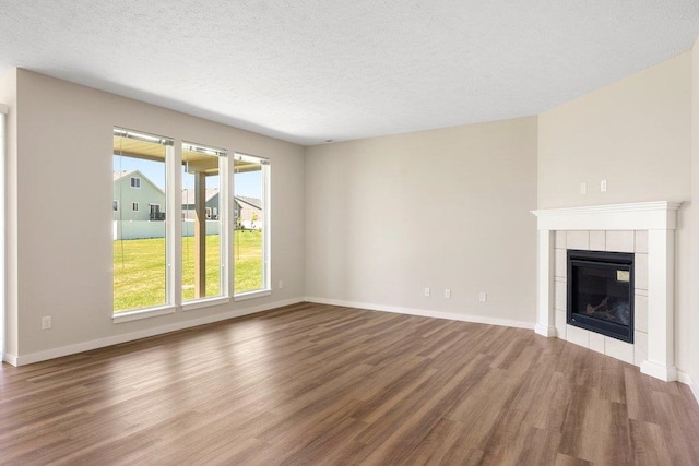 unfurnished living room with wood finished floors, a tiled fireplace, a textured ceiling, and baseboards