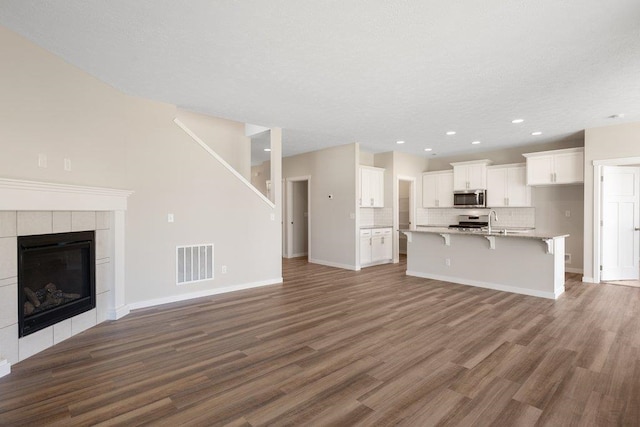 unfurnished living room featuring a sink, wood finished floors, recessed lighting, baseboards, and a tiled fireplace