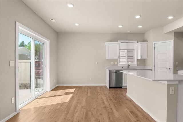 kitchen with stainless steel dishwasher, light wood-style floors, a sink, light countertops, and white cabinetry