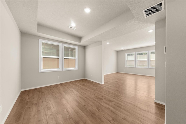 empty room with light wood-type flooring, recessed lighting, baseboards, a textured ceiling, and a tray ceiling