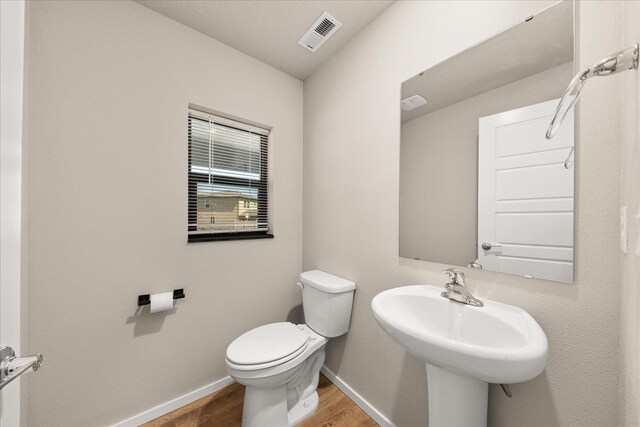 half bathroom featuring wood finished floors, toilet, baseboards, and a sink