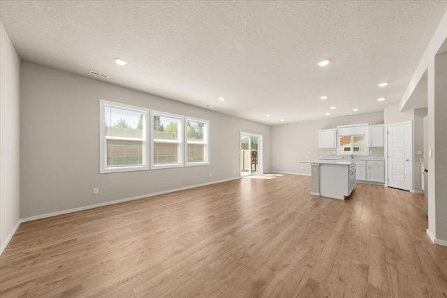 unfurnished living room with light wood-style floors, a textured ceiling, baseboards, and recessed lighting