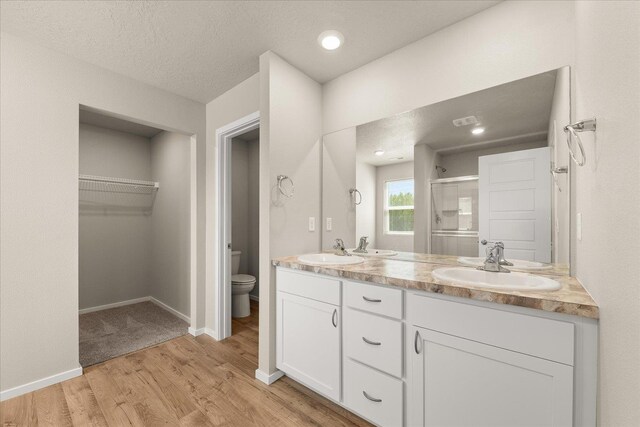 full bathroom featuring toilet, a stall shower, wood finished floors, double vanity, and a spacious closet