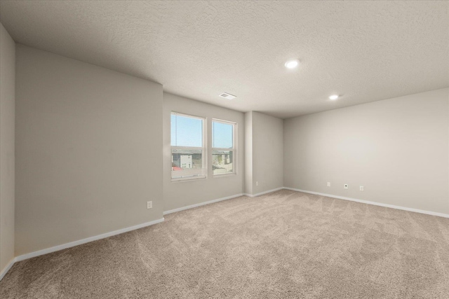 empty room with light colored carpet, a textured ceiling, baseboards, and recessed lighting