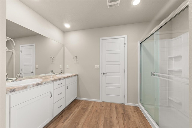 bathroom featuring a shower stall, wood finished floors, double vanity, baseboards, and recessed lighting