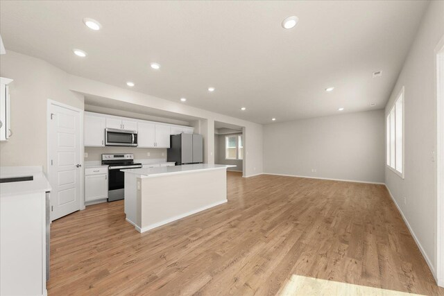 kitchen with stainless steel appliances, a center island, white cabinets, light wood-style floors, and recessed lighting