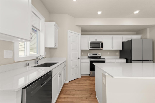 kitchen with appliances with stainless steel finishes, a sink, light wood-style flooring, white cabinets, and recessed lighting