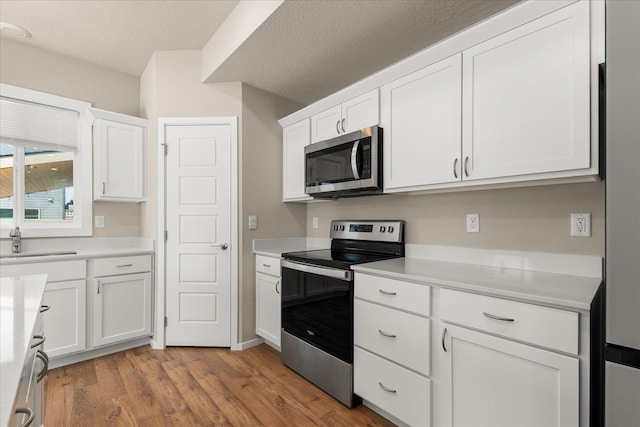 kitchen with appliances with stainless steel finishes, a sink, white cabinetry, light countertops, and a textured ceiling