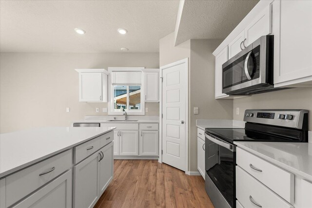 kitchen with stainless steel appliances, light countertops, light wood finished floors, white cabinets, and recessed lighting