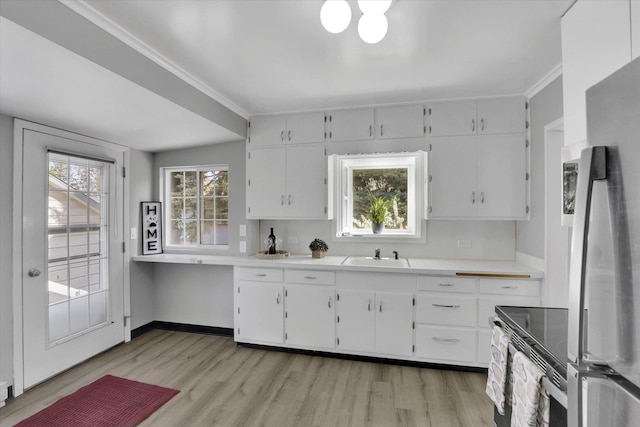 kitchen with freestanding refrigerator, a sink, white cabinets, light wood-type flooring, and ornamental molding