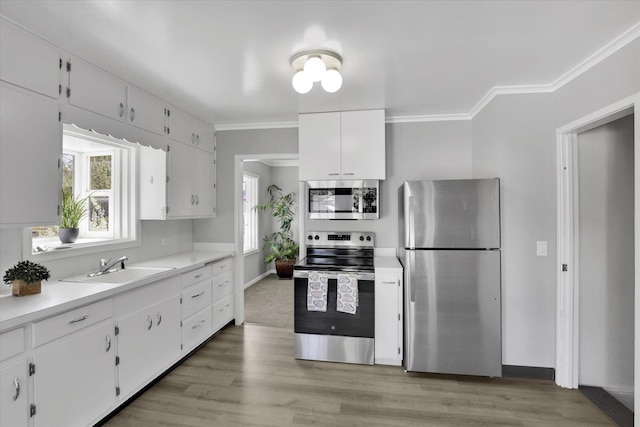 kitchen with appliances with stainless steel finishes, healthy amount of natural light, white cabinets, crown molding, and a sink