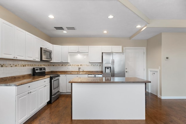 kitchen featuring stainless steel appliances, backsplash, a kitchen island, a sink, and white cabinets