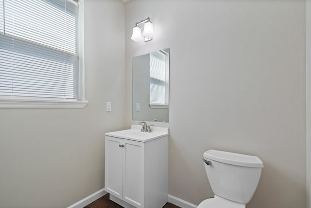 half bathroom with baseboards, vanity, and toilet