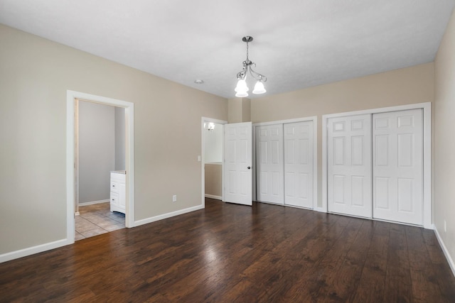 unfurnished bedroom featuring two closets, wood finished floors, baseboards, and a chandelier