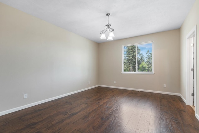 empty room featuring dark wood-type flooring, baseboards, and a chandelier