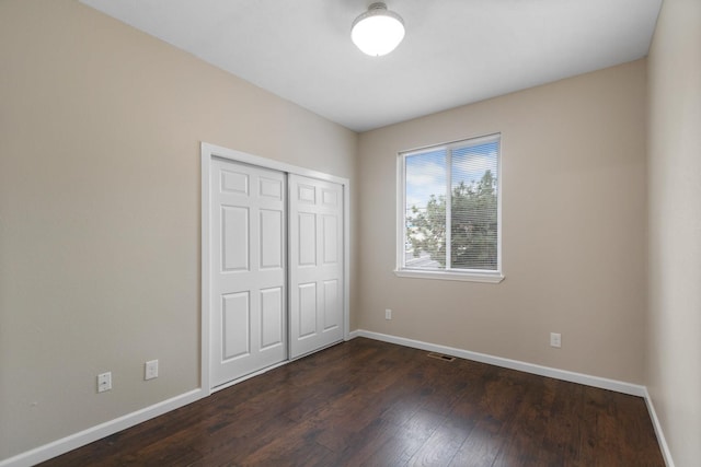 unfurnished bedroom with baseboards, dark wood-style flooring, and a closet