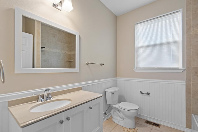 bathroom with a wainscoted wall, tiled shower, vanity, toilet, and tile patterned flooring