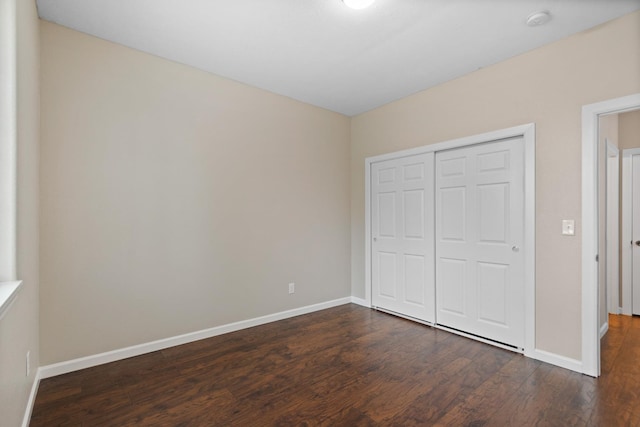 unfurnished bedroom with dark wood finished floors, baseboards, and a closet