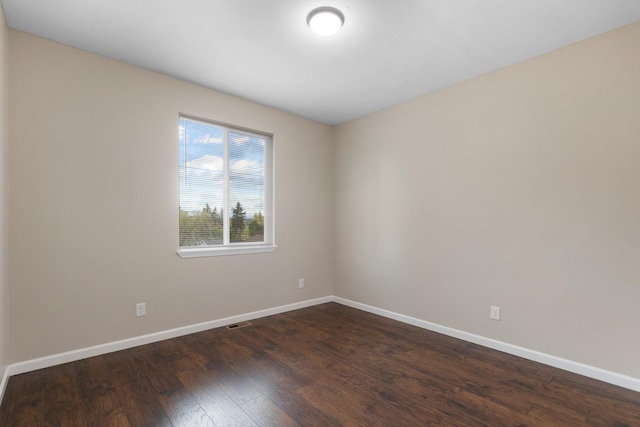spare room with baseboards and dark wood-type flooring