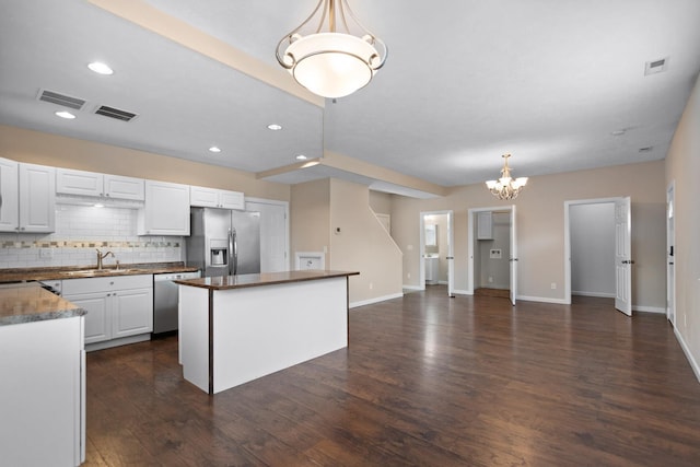 kitchen with stainless steel appliances, a sink, dark countertops, a chandelier, and decorative backsplash