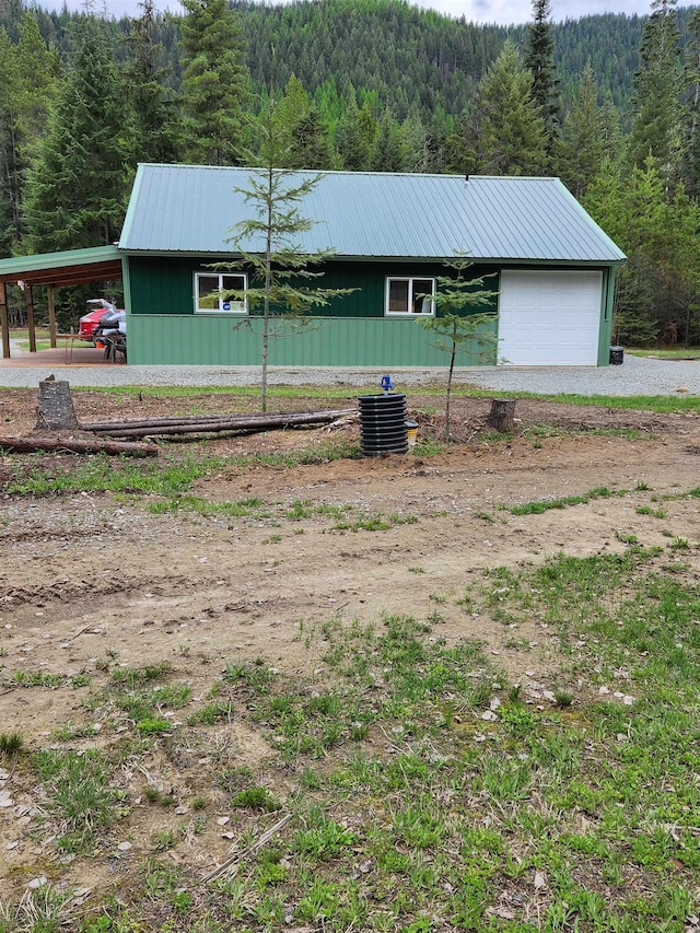 view of home's exterior with a wooded view, metal roof, and driveway