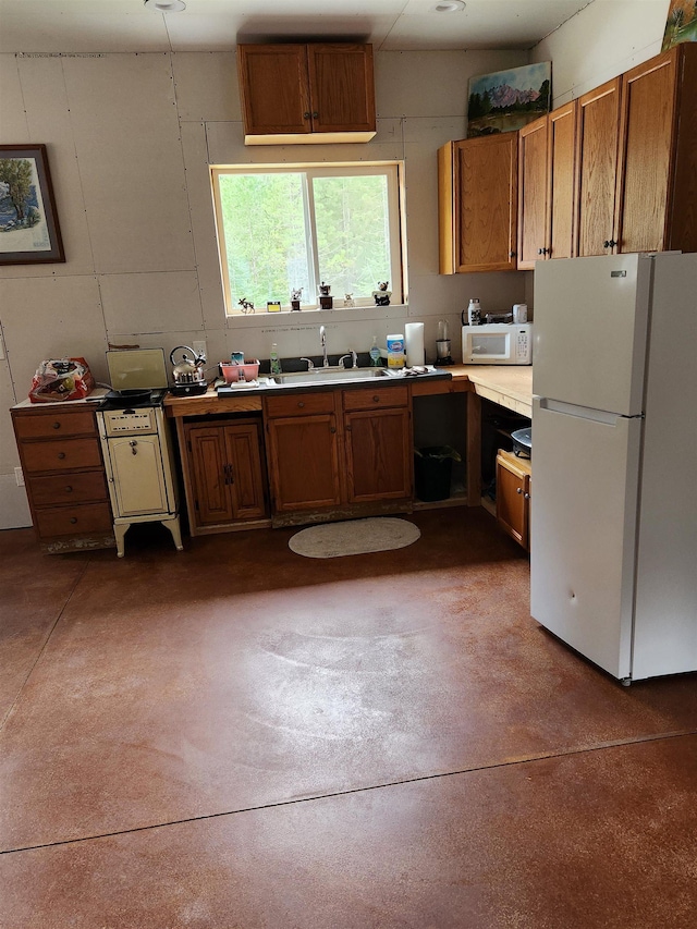 kitchen with white appliances, concrete floors, brown cabinets, a sink, and light countertops