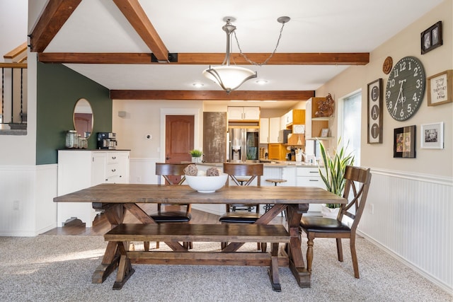 carpeted dining space with beamed ceiling and wainscoting
