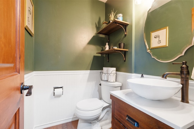 half bath with a wainscoted wall, toilet, vanity, and wood finished floors