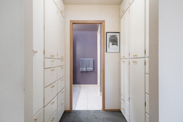 hallway featuring baseboards, light tile patterned floors, and light carpet