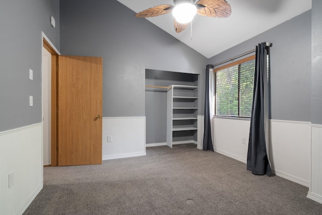 unfurnished bedroom with wainscoting, carpet flooring, a closet, ceiling fan, and high vaulted ceiling