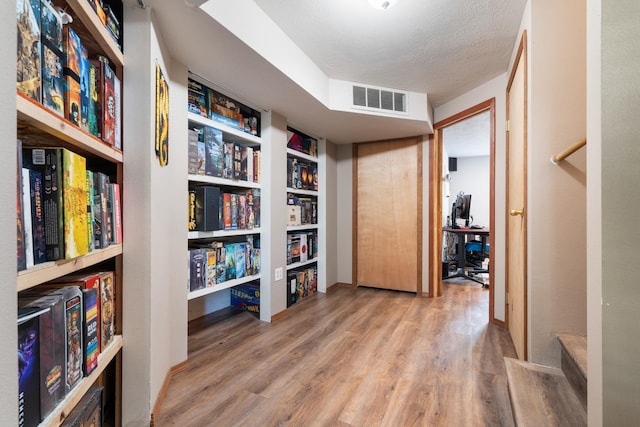 hall featuring wood finished floors, built in features, and a textured ceiling