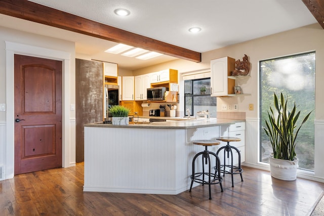 kitchen featuring stainless steel microwave, beam ceiling, dark wood finished floors, a peninsula, and a kitchen bar
