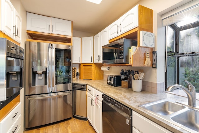 kitchen with stainless steel appliances, a sink, white cabinets, light wood finished floors, and vaulted ceiling