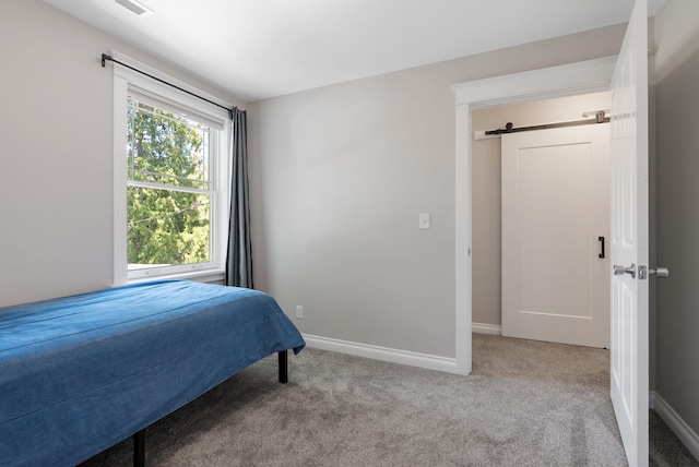 carpeted bedroom featuring a barn door and baseboards