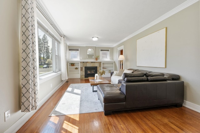 living room with wood finished floors, a tile fireplace, crown molding, and baseboards