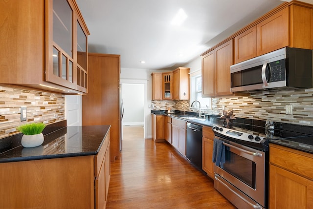 kitchen with stainless steel appliances, backsplash, light wood-style flooring, a sink, and dark stone countertops