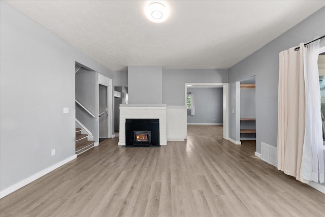 unfurnished living room featuring stairway, light wood-type flooring, baseboards, and a textured ceiling