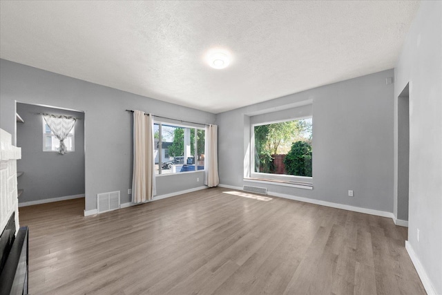 unfurnished living room featuring wood finished floors, a textured ceiling, a fireplace, and baseboards