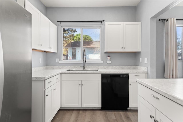 kitchen with black dishwasher, a sink, freestanding refrigerator, light countertops, and white cabinetry