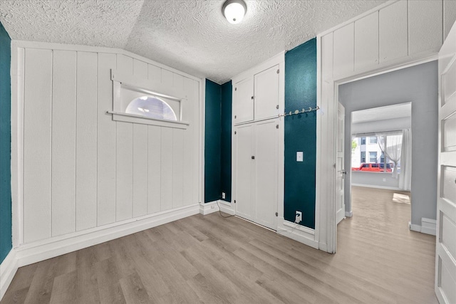 entryway with light wood-style floors, a textured ceiling, baseboards, and vaulted ceiling