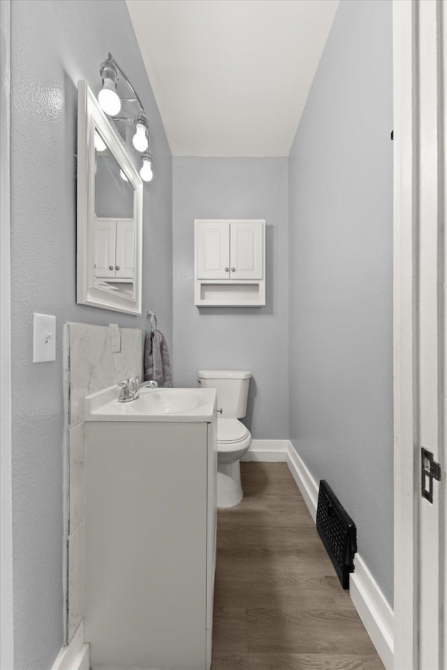 bathroom featuring baseboards, toilet, wood finished floors, and vanity