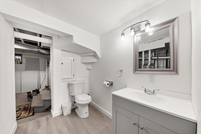 bathroom with wood finished floors, toilet, vanity, and baseboards