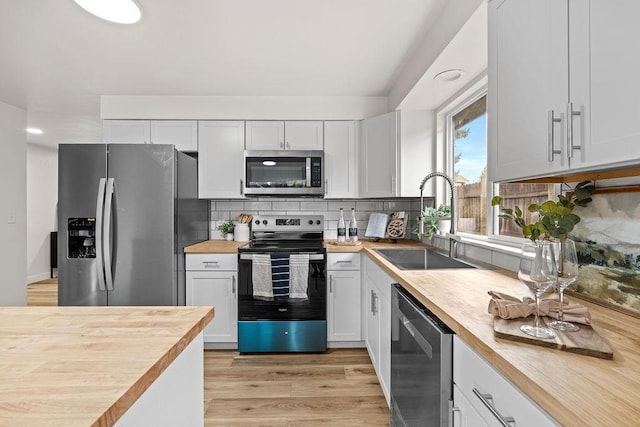 kitchen featuring stainless steel appliances, butcher block countertops, a sink, decorative backsplash, and light wood-style floors